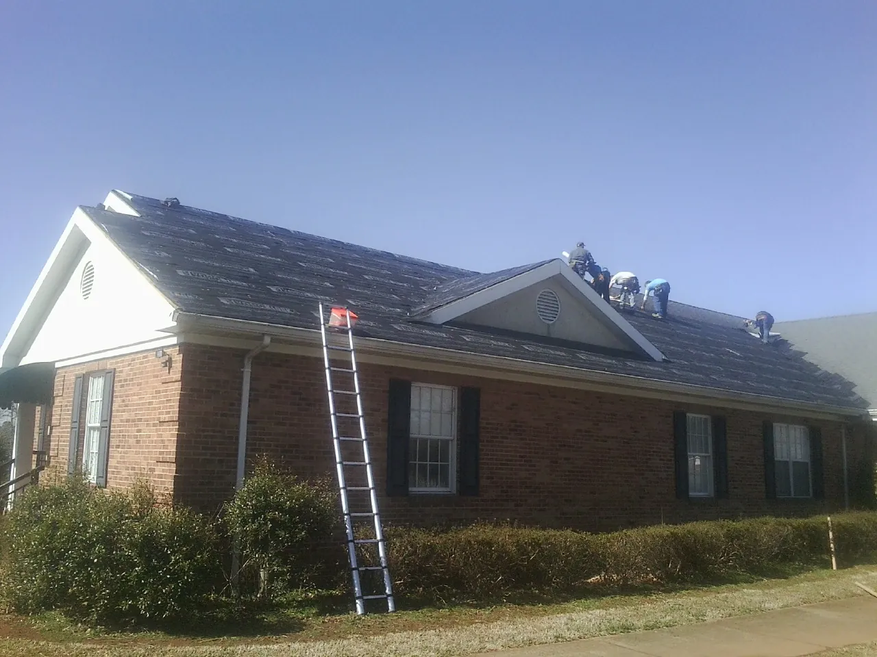 Crew tearing shingles off a brick ranch roof with a ladder set — Emergency Roof Repair work by our crew in Merrimack
