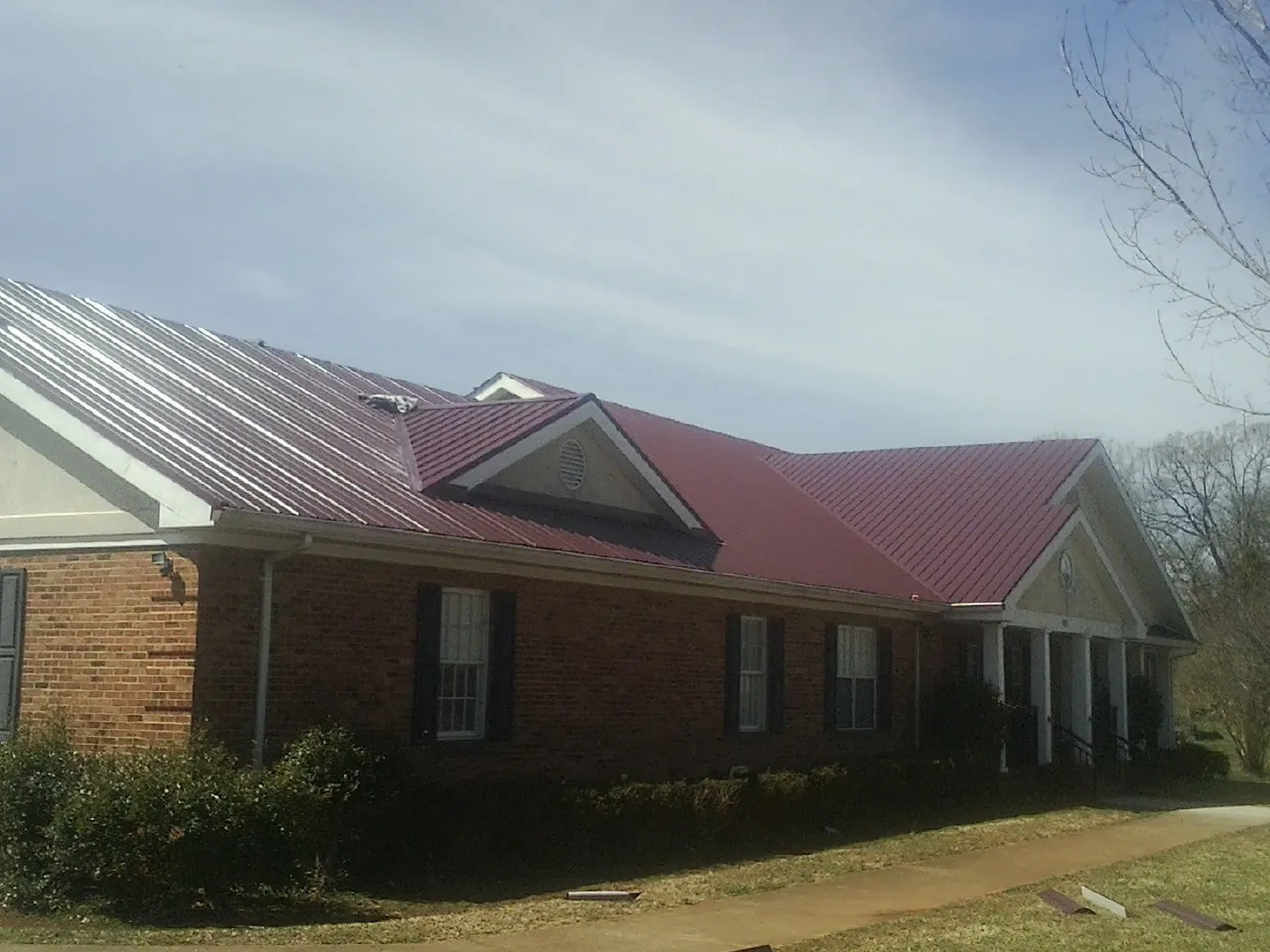 Red metal roof with gabled entries on a long brick building, from a Hail Damage Roof Repair job in Merrimack