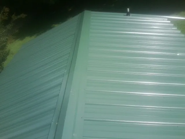 New green metal panels meeting at the ridge of a roof — Flat Roof Repair work by our crew in Merrimack