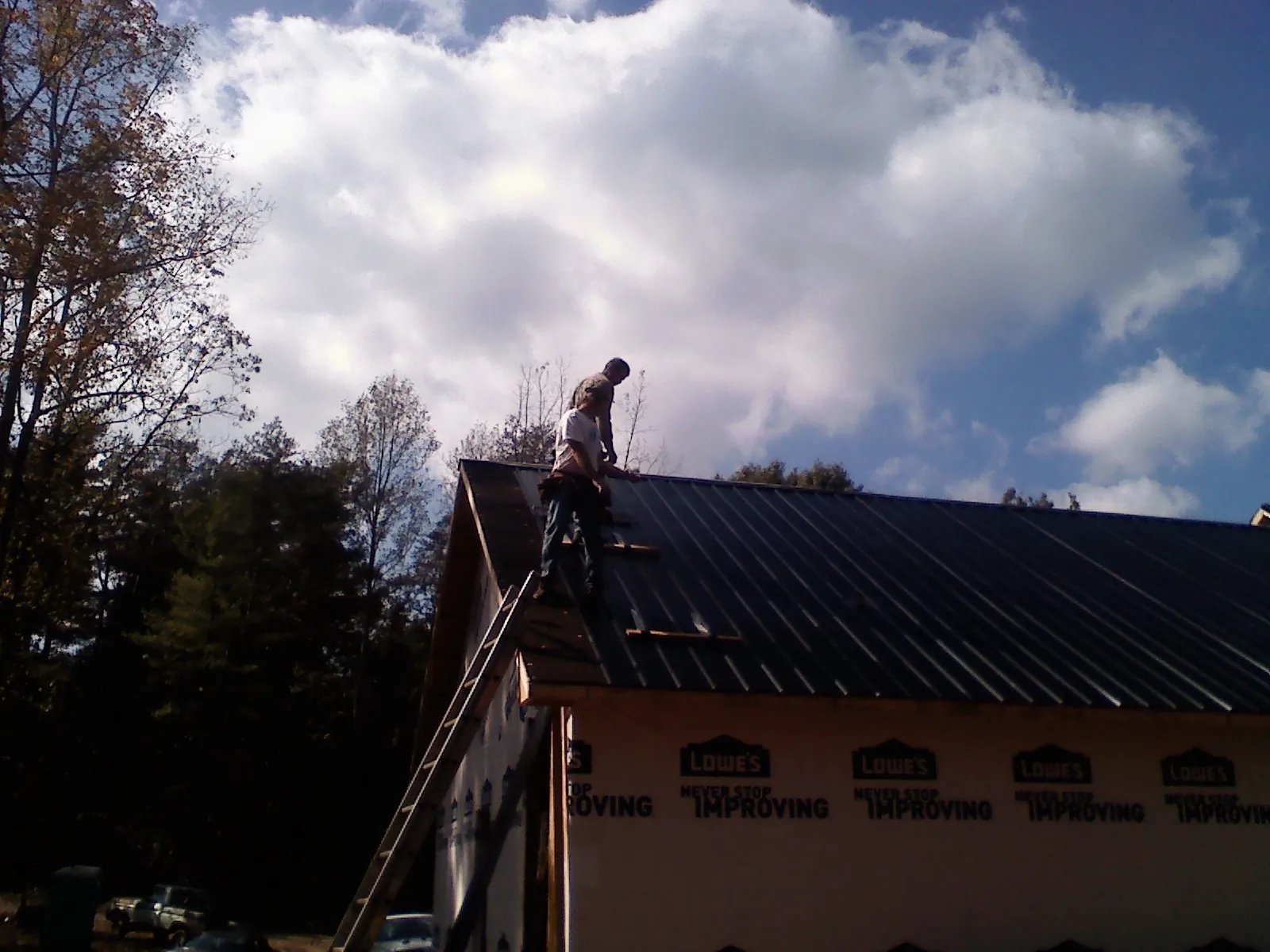 Roofer fastening dark metal panels high against a cloudy sky, from a Roof Inspection job in Merrimack