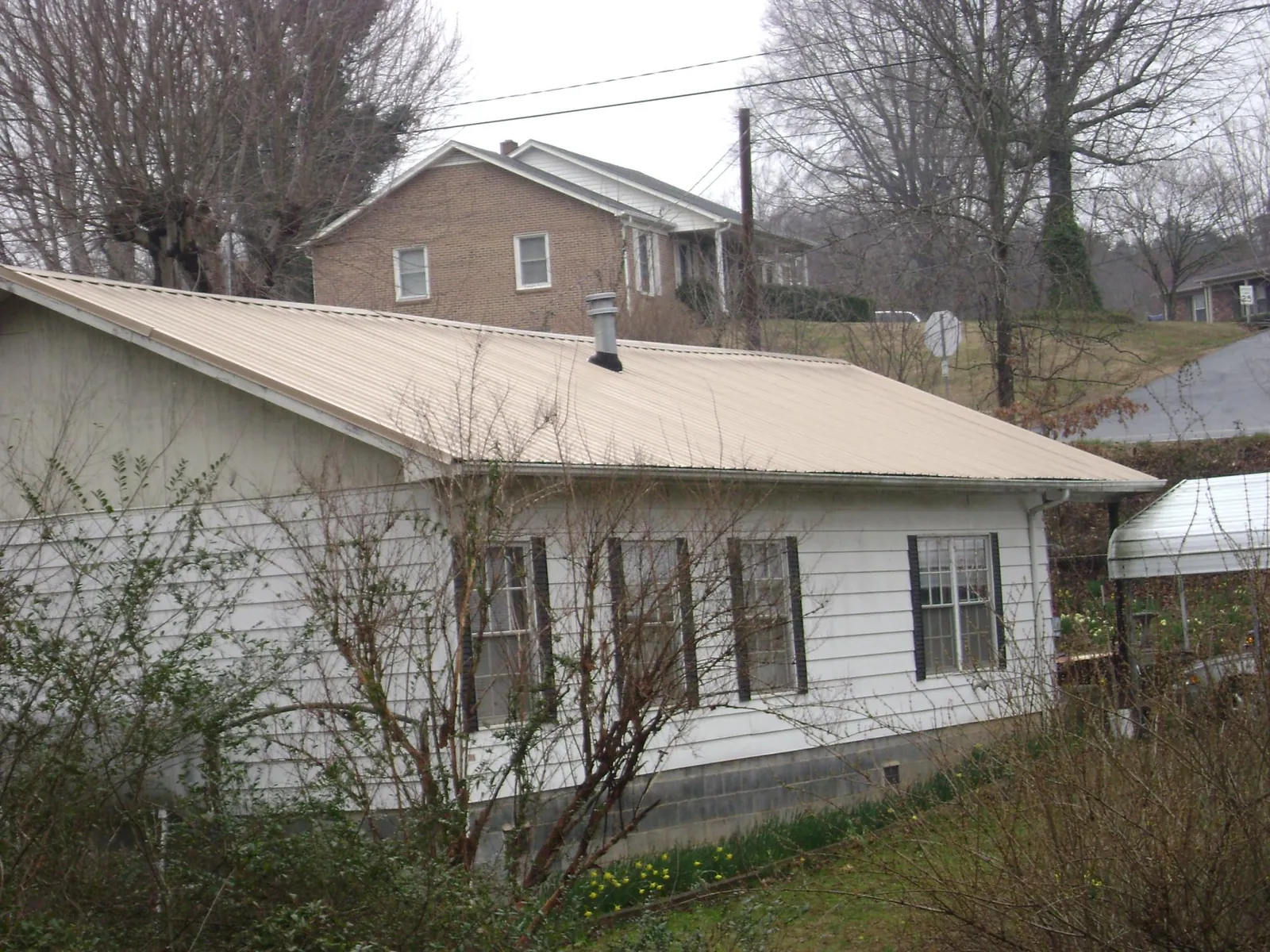 Tan metal roof on a white sided house set into a hillside — Commercial Roofing by Roofing Brothers in Merrimack