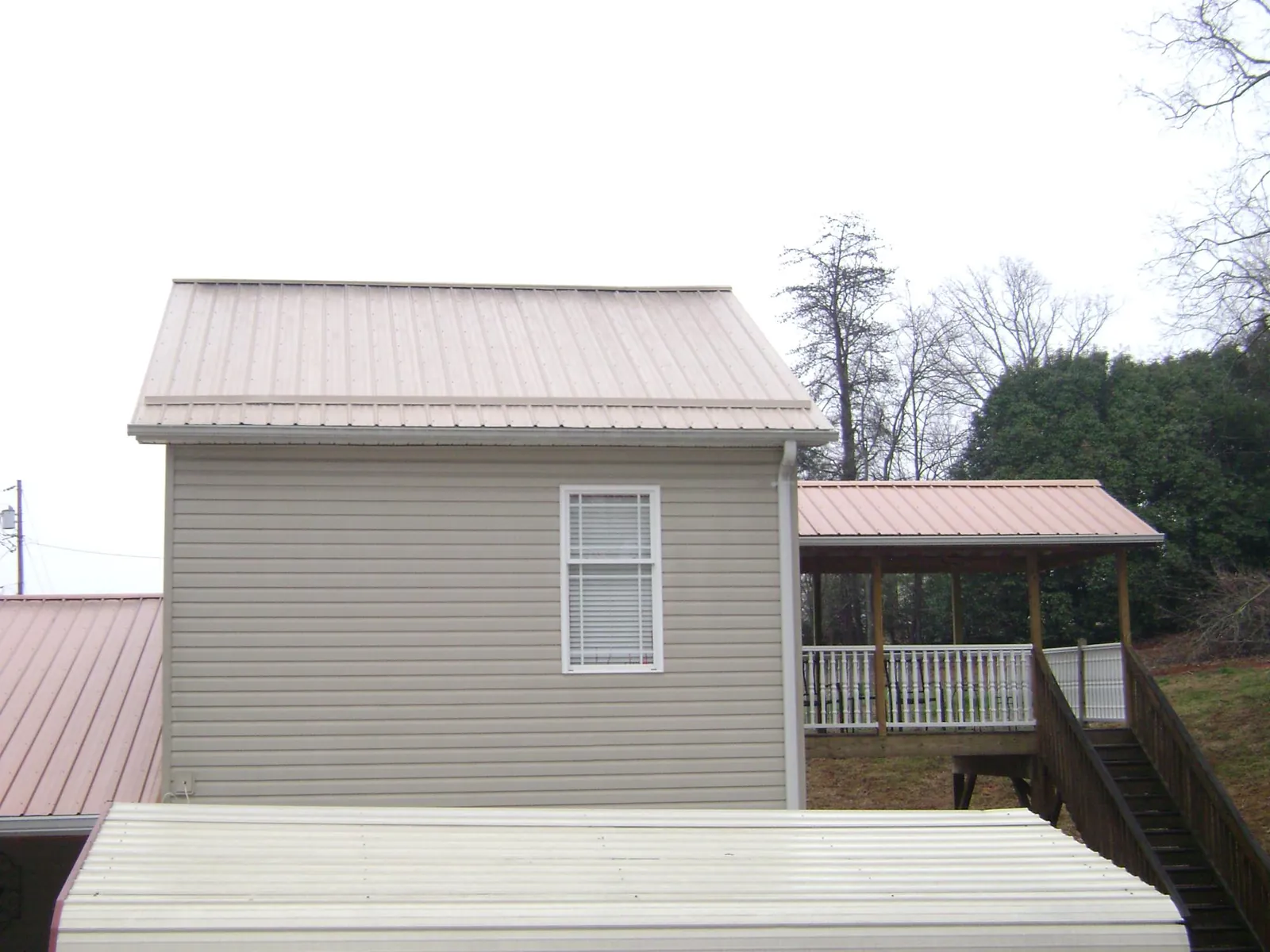 Tan metal roofs on a two story addition and attached porch, from a Roof Replacement job in Merrimack